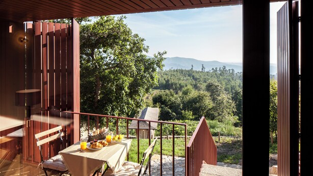 Un espace de restauration en plein air avec une table dressée pour deux personnes, offrant une vue sur un paysage boisé.