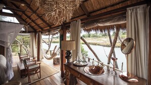 Une pièce au décor rustique, avec des meubles en bois, une grande fenêtre donnant sur un lac, une lampe suspendue et un lavabo rustique.