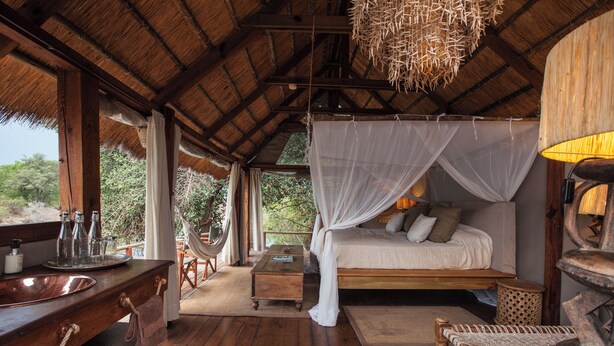 Une chambre à coucher rustique avec un lit en bois, un bureau en bois, une lampe de chevet et une vue sur l’extérieur.