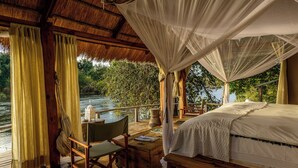 Une terrasse en bois avec un lit, une table et une chaise, donnant sur une rivière.