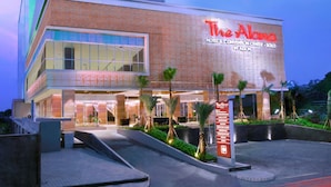 El Hotel y Centro de Convenciones Alona, con fachada moderna, ventanas amplias y un área de entrada bien iluminada con palmeras.