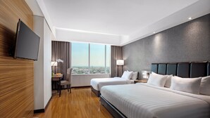Habitación de hotel moderna con dos camas, un escritorio, una silla, un televisor y un ventanal con vistas a la ciudad.