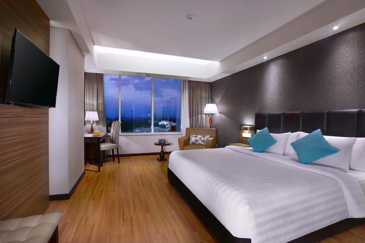 Une chambre d’hôtel avec un grand lit, un bureau avec une chaise, un téléviseur fixé au mur et une fenêtre donnant sur la ville.