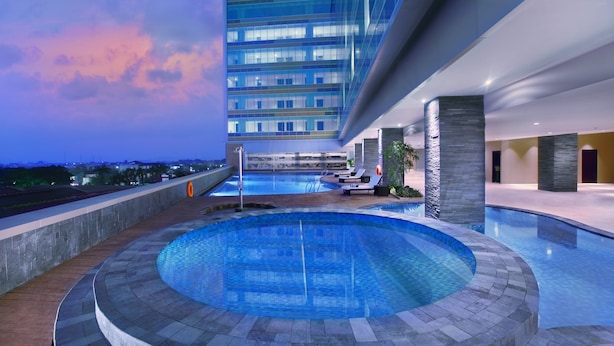Un hotel moderno con piscina infinita en la azotea, vistas del perfil urbano y un gran edificio con ventanas de vidrio reflectante.