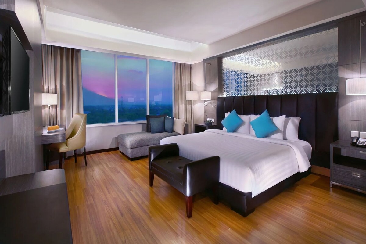 Habitación de hotel moderna con una cama grande, un escritorio, una silla y vistas de la ciudad.