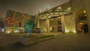 Una entrada de hotel moderna con una fachada geométrica distintiva, un espacio exterior cubierto y un estacionamiento.