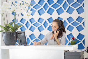 Un mostrador de recepción con una planta en maceta, una computadora y una persona escribiendo.