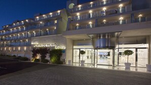 A multi-story hotel with a prominent entrance, large potted plants, and a well-lit facade. - Mar Hotels Playa de Muro Suites (Muro)