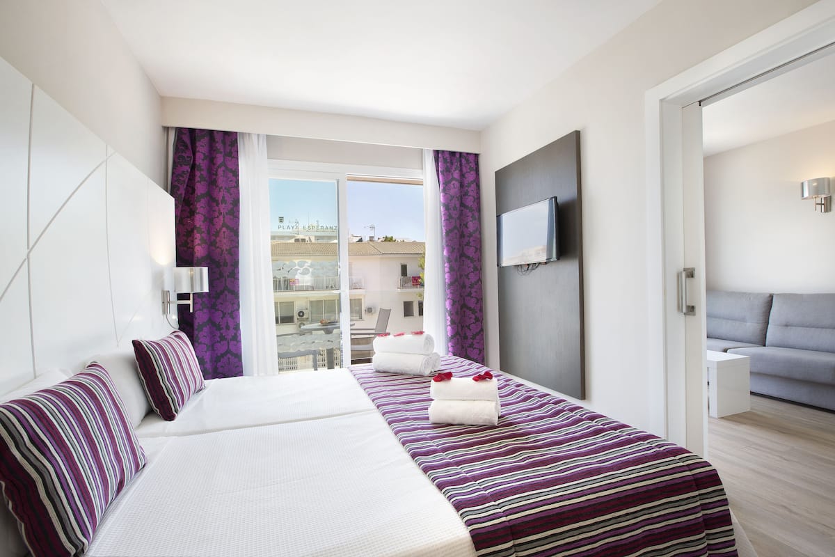 Una habitación de hotel moderna con una cama grande, un sofá, un televisor y un balcón con vistas a la ciudad.