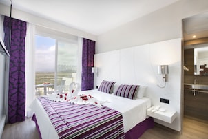 Una habitación de hotel moderna con una cama grande, una mesita de noche con un teléfono y vistas al paisaje por la ventana.