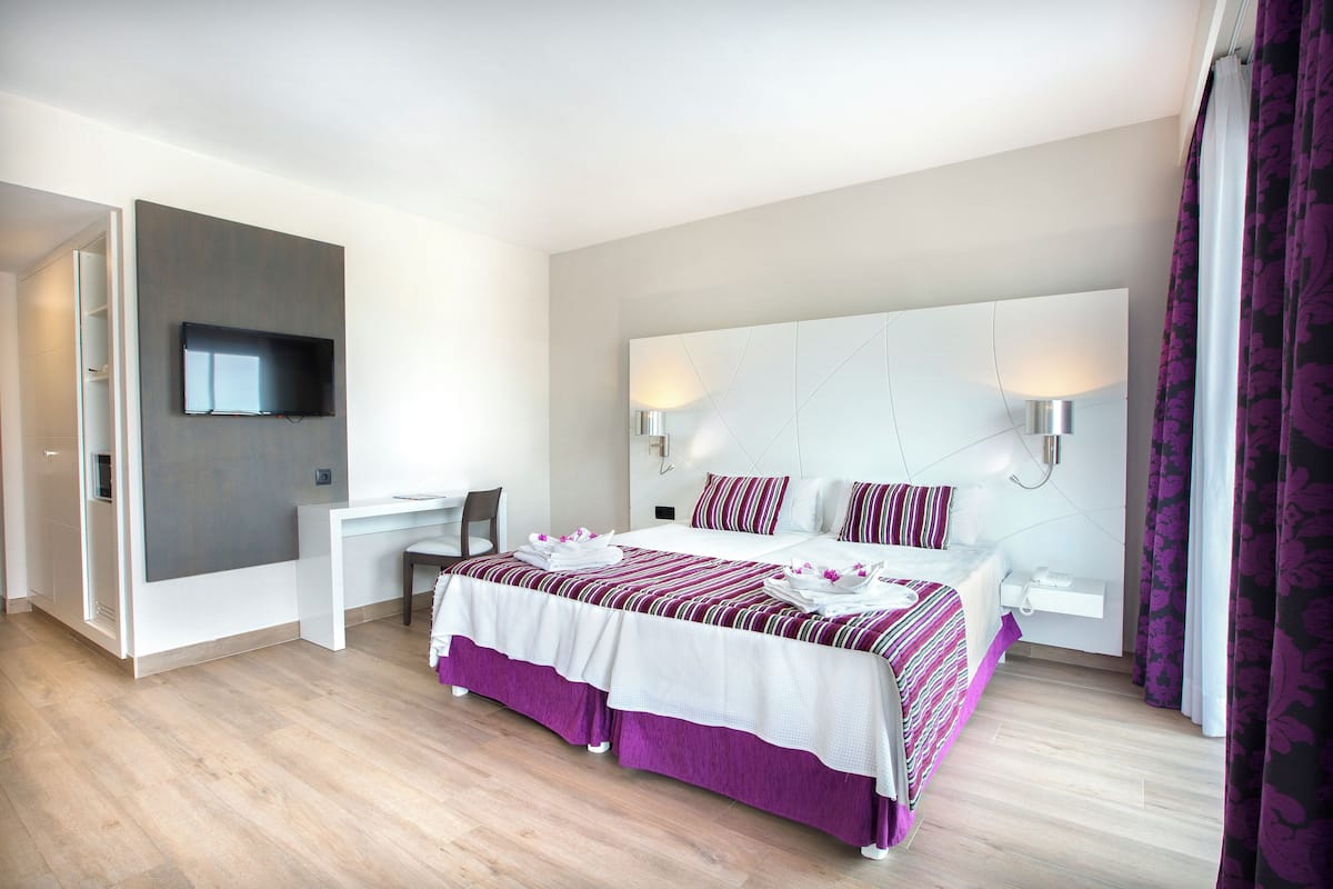 Habitación de hotel moderna con una cama grande, un escritorio y un televisor de pantalla plana montado en la pared.