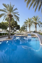 Una piscina con palmeras y sillas de descanso.