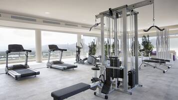 Un gimnasio con cintas de correr, elípticas, banco y equipo de levantamiento de pesas.