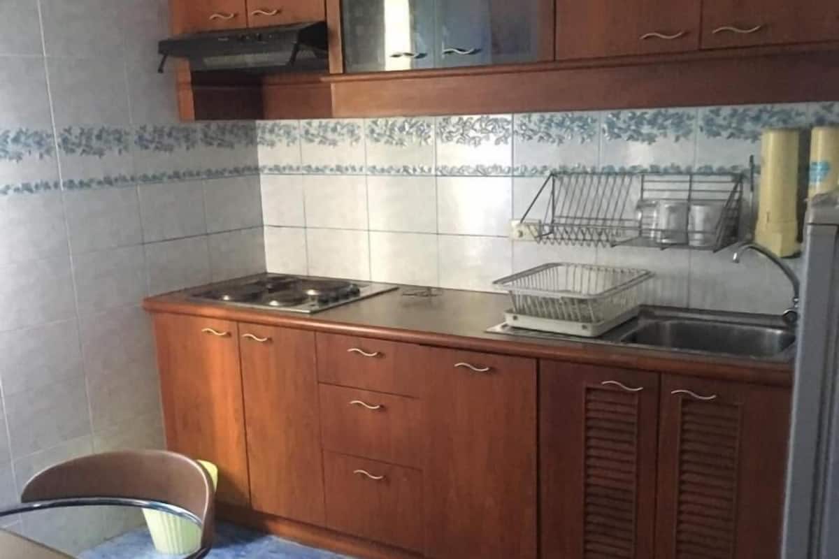 A kitchen with wooden cabinets, a gas stove, a sink, and a chair.