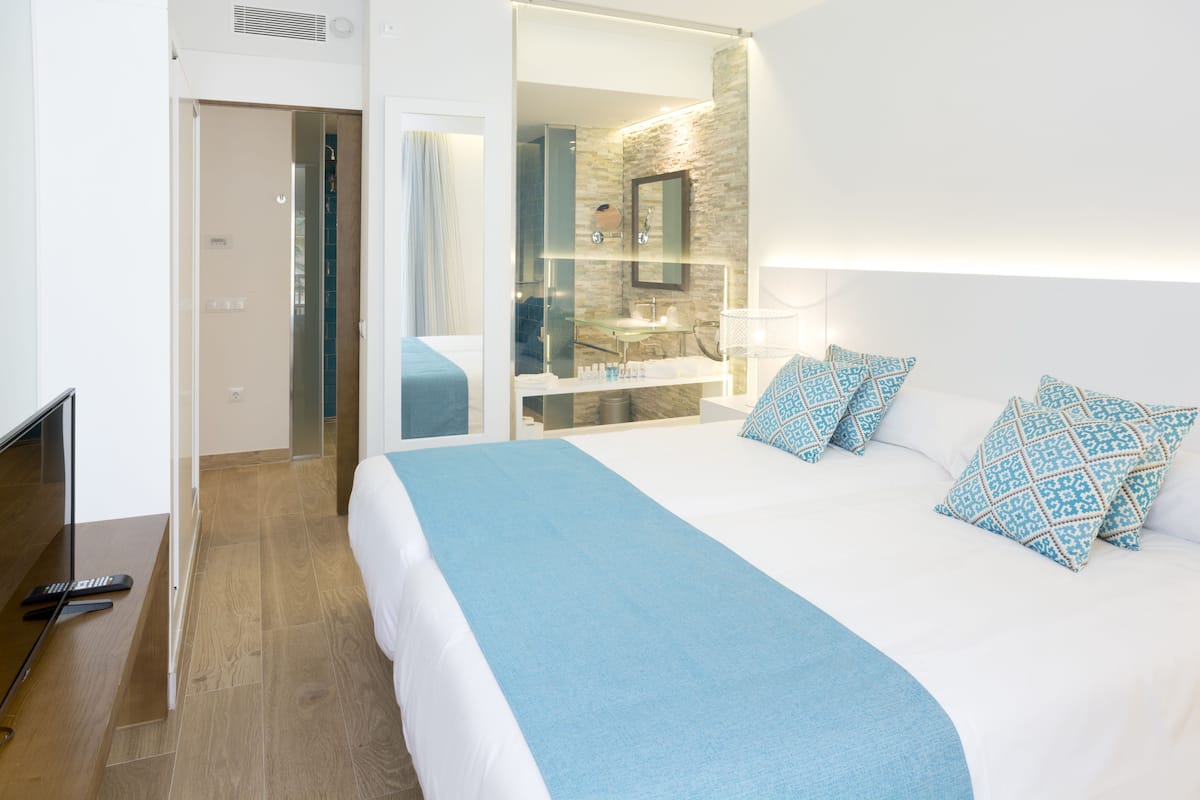 Habitación de hotel con una cama grande, baño con ducha de vidrio y televisor de pantalla plana.