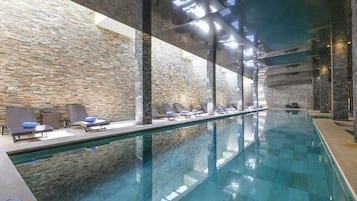 Une piscine intérieure moderne, avec des murs en pierre et des chaises longues disposées le long des bords.