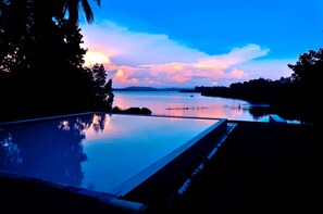 Une piscine à débordement paisible, offrant une vue dégagée sur un lac calme et des montagnes lointaines au coucher du soleil.