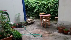 Een terras met stenen bestrating, plantenpotten, een houten bank en een tafel met stoelen.