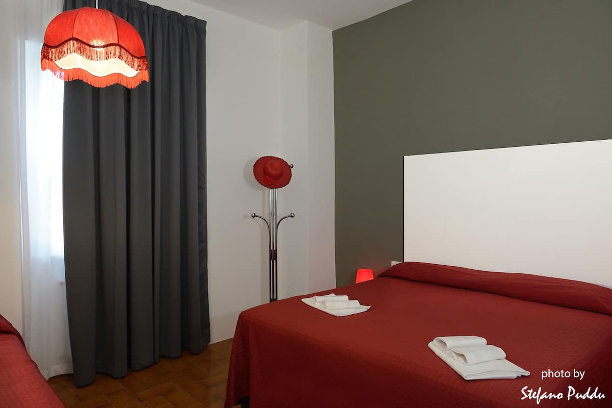 Ein Hotelzimmer mit einem Bett, einer roten Bettdecke, einem weißen Kopfteil, einer roten Lampe und einem roten Hut auf einem Sockel.