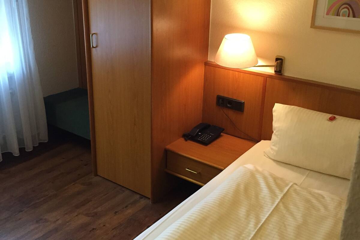 A hotel room with a bed, a nightstand, a lamp, a phone, and a wardrobe.