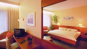 Habitación de hotel con cama, escritorio con televisor, silla, espejo y planta.