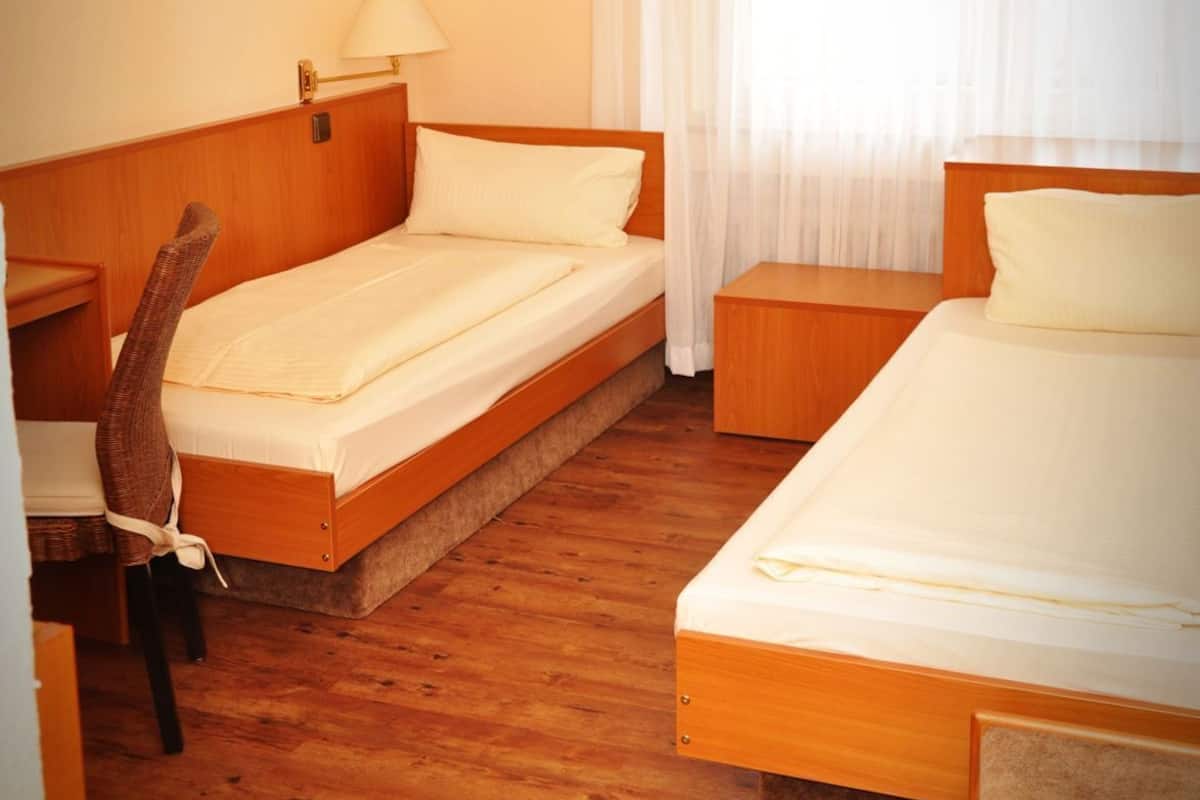 A hotel room with two beds, a desk, a chair, a lamp, and a window with curtains.
