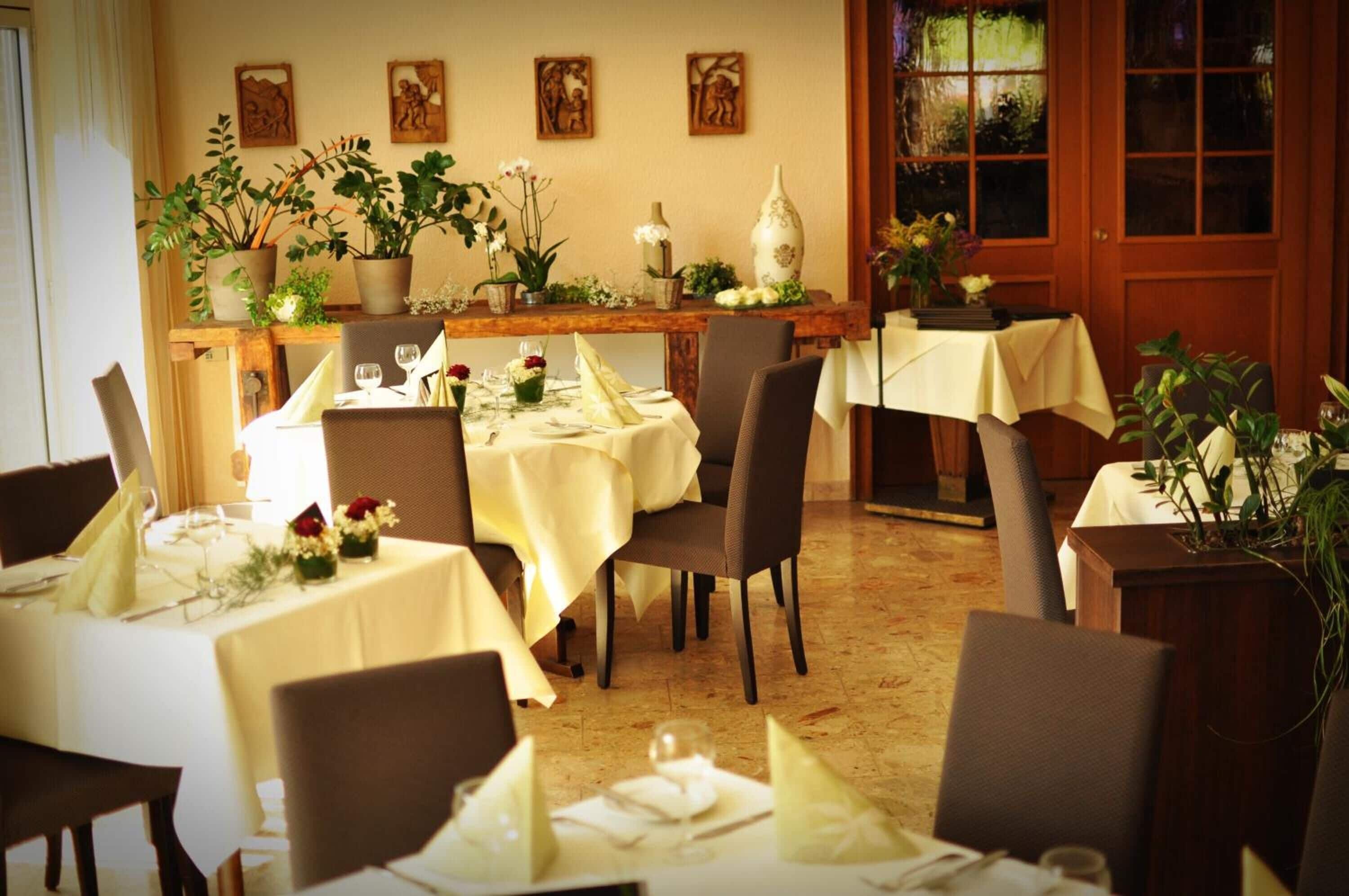 Un comedor con varias mesas dispuestas para una comida, cada una con manteles blancos y centros de mesa florales.