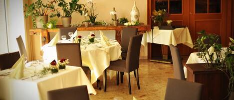 Un comedor con varias mesas dispuestas para una comida, cada una con manteles blancos y centros de mesa florales.
