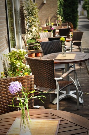 An outdoor seating area with wicker chairs and tables, surrounded by potted plants and flowers. - Hotel Litjes (Goch)