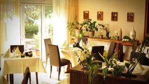 Un comedor con mesas dispuestas para dos, plantas en macetas y obras de arte en la pared.