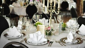 Una mesa de comedor formal vestida con manteles blancos, cubiertos y cristalería, rodeada de sillas negras.
