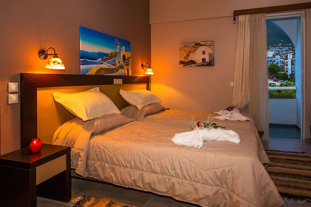 A hotel room with two beds, a nightstand with a red vase, and artwork on the walls.