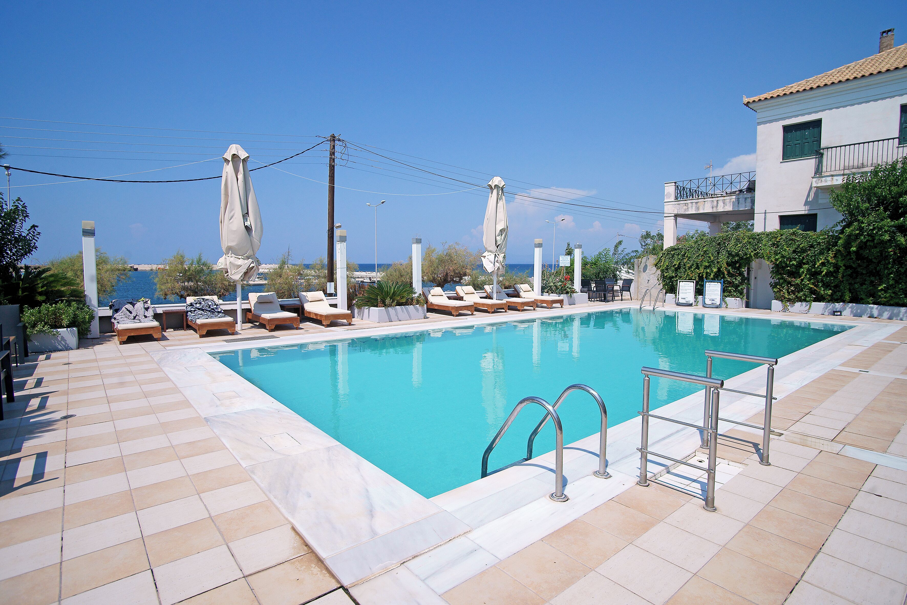 A swimming pool with lounge chairs and umbrellas, a clear sky, and a building in the background.
