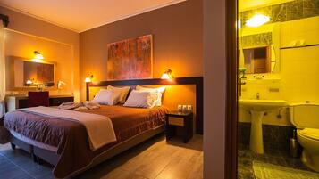 A hotel room with a bed, bedside lamps, a painting on the wall, a desk with a lamp, and a bathroom with a sink and toilet.