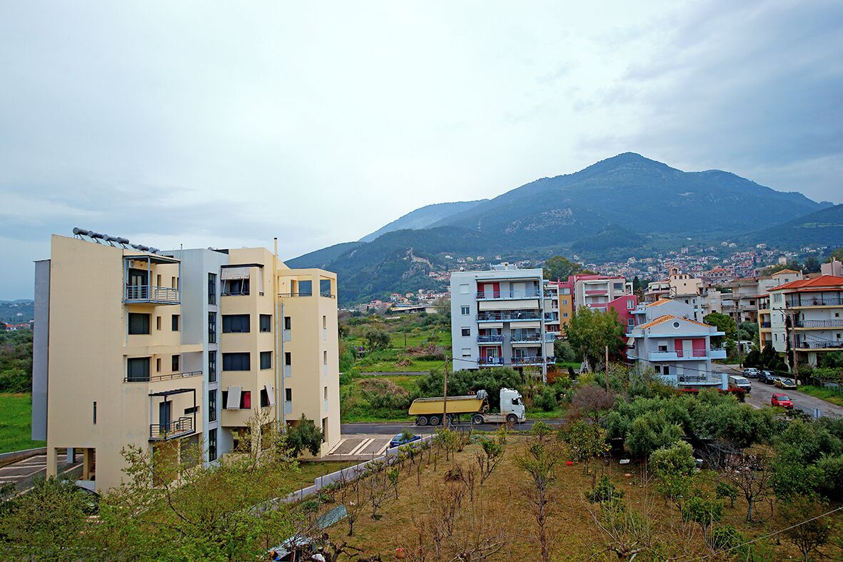 A residential area with multi-story buildings, a truck on the road, and a mountain in the background.