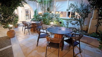 An outdoor patio area with a round table and chairs, surrounded by potted plants and a tiled floor.