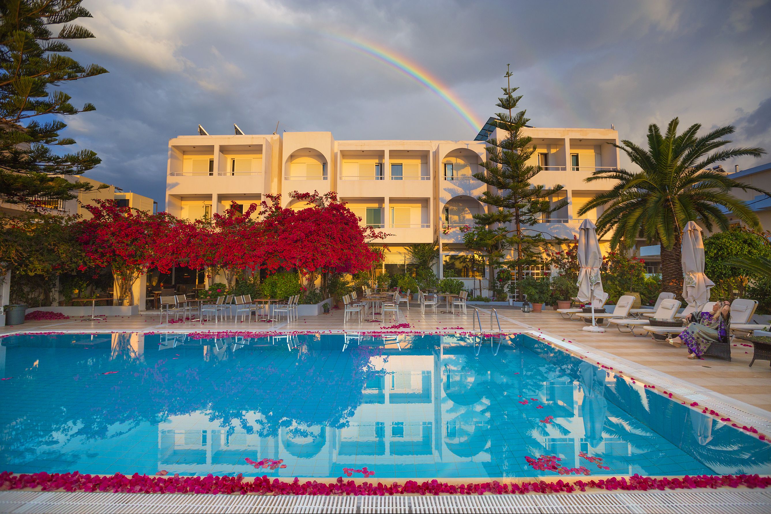 A swimming pool with a reflection of a building and a rainbow in the background.