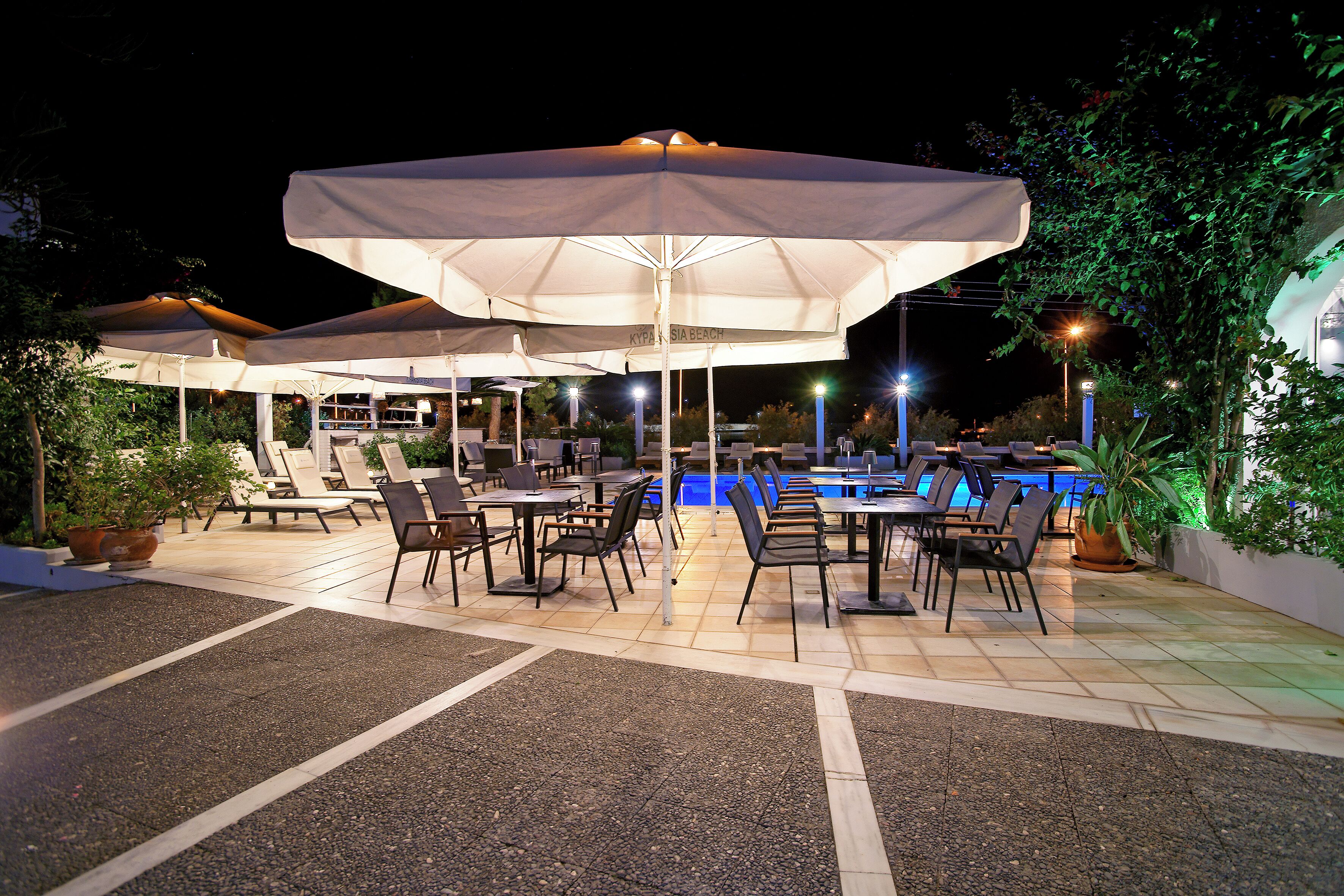 An outdoor pool area with multiple umbrellas, lounge chairs, and dining tables.