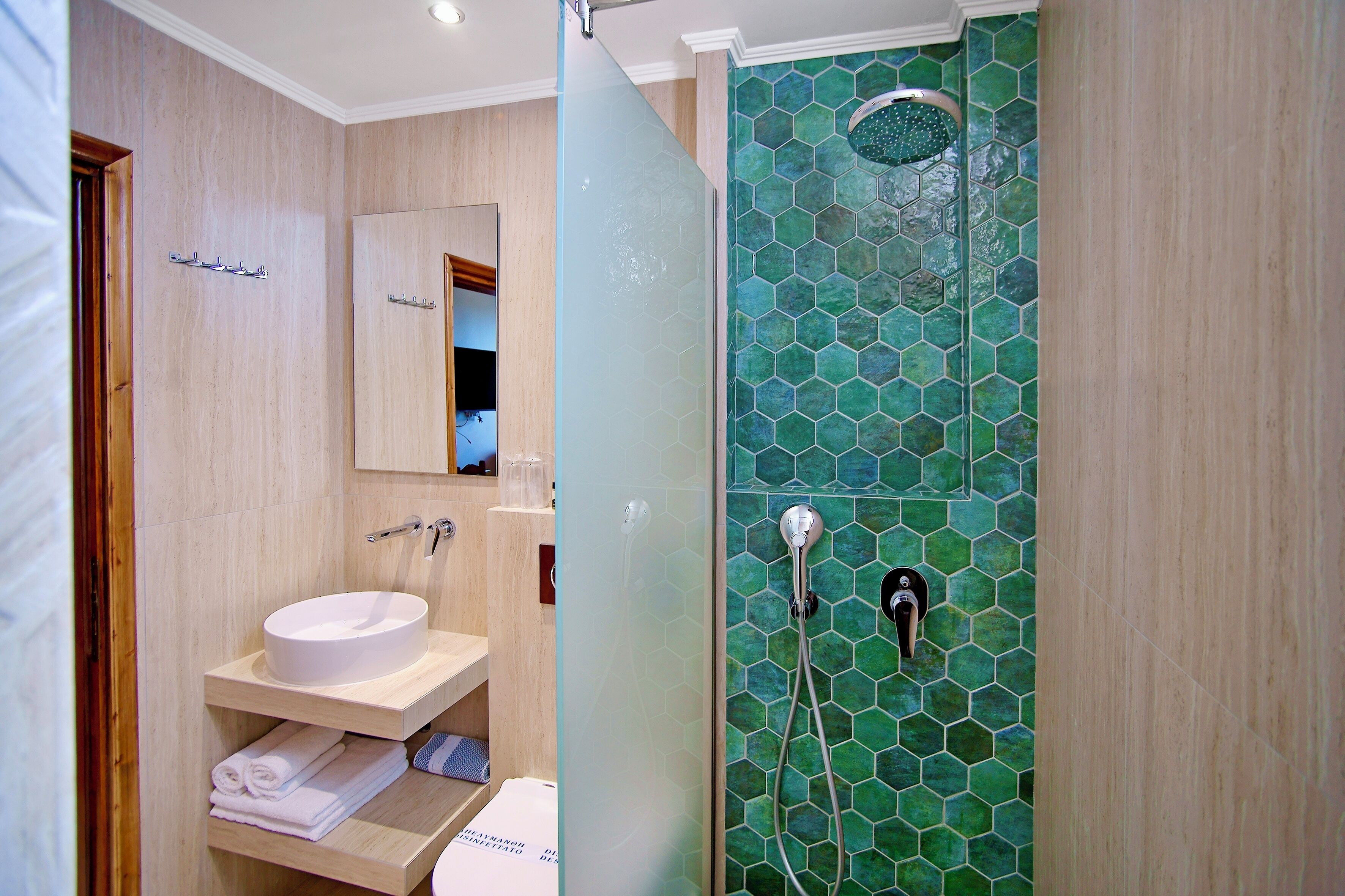 Un baño con un lavabo blanco, un espejo y una ducha con baldosas hexagonales verdes.