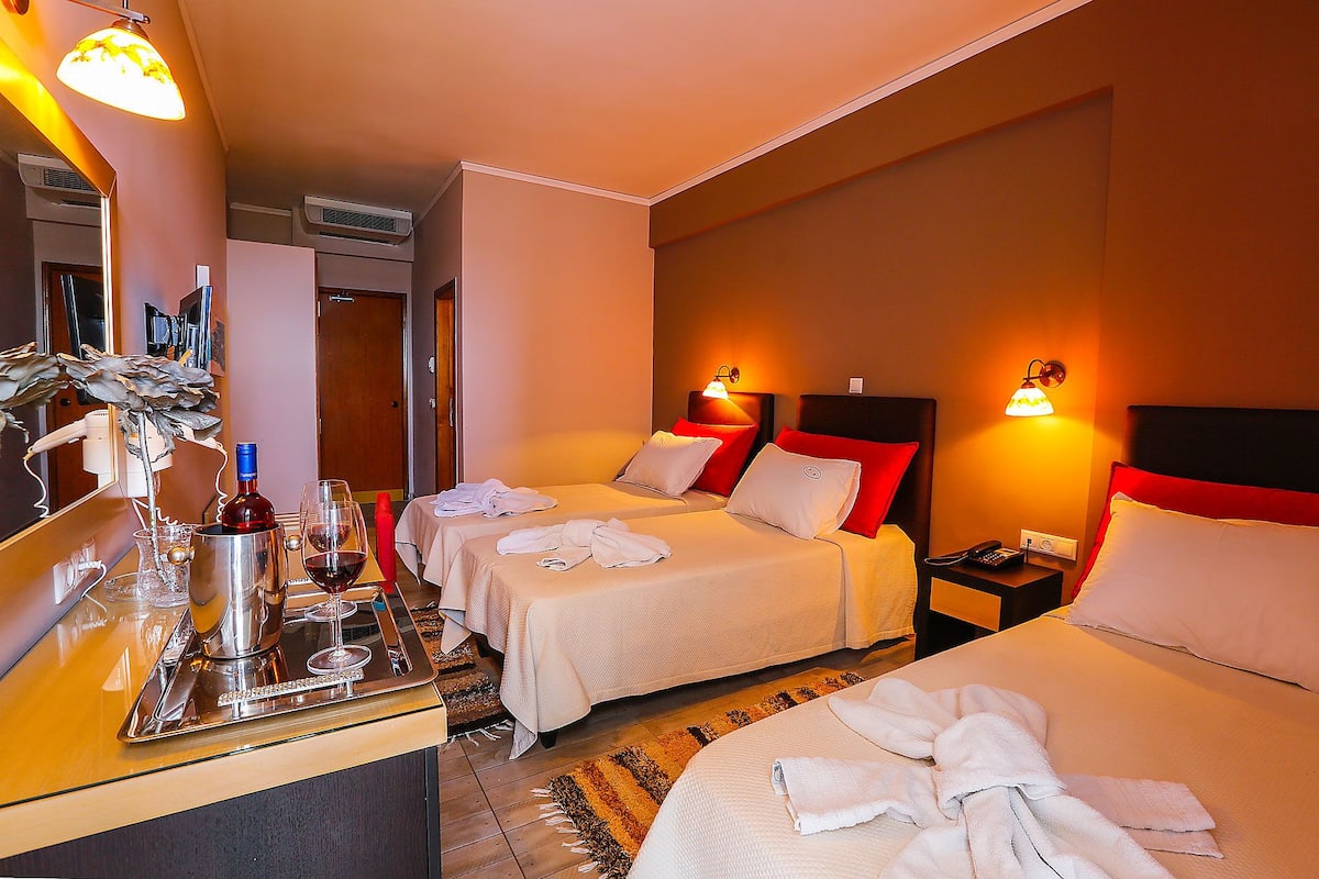 A hotel room with two beds, a minibar, a mirror, and a bathroom visible in the background.