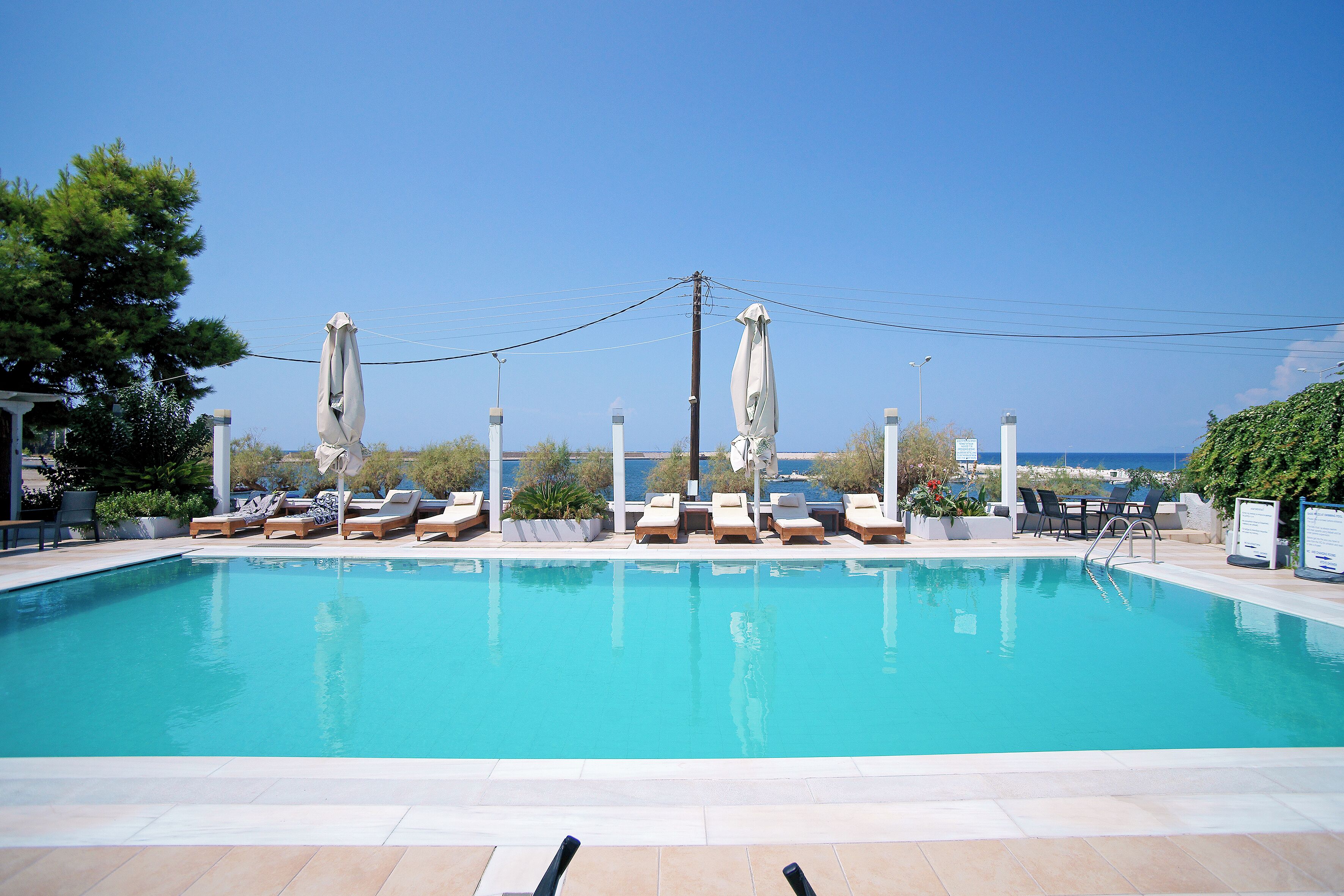 Une piscine entourée de chaises longues et de parasols, avec un ciel dégagé et une végétation luxuriante.