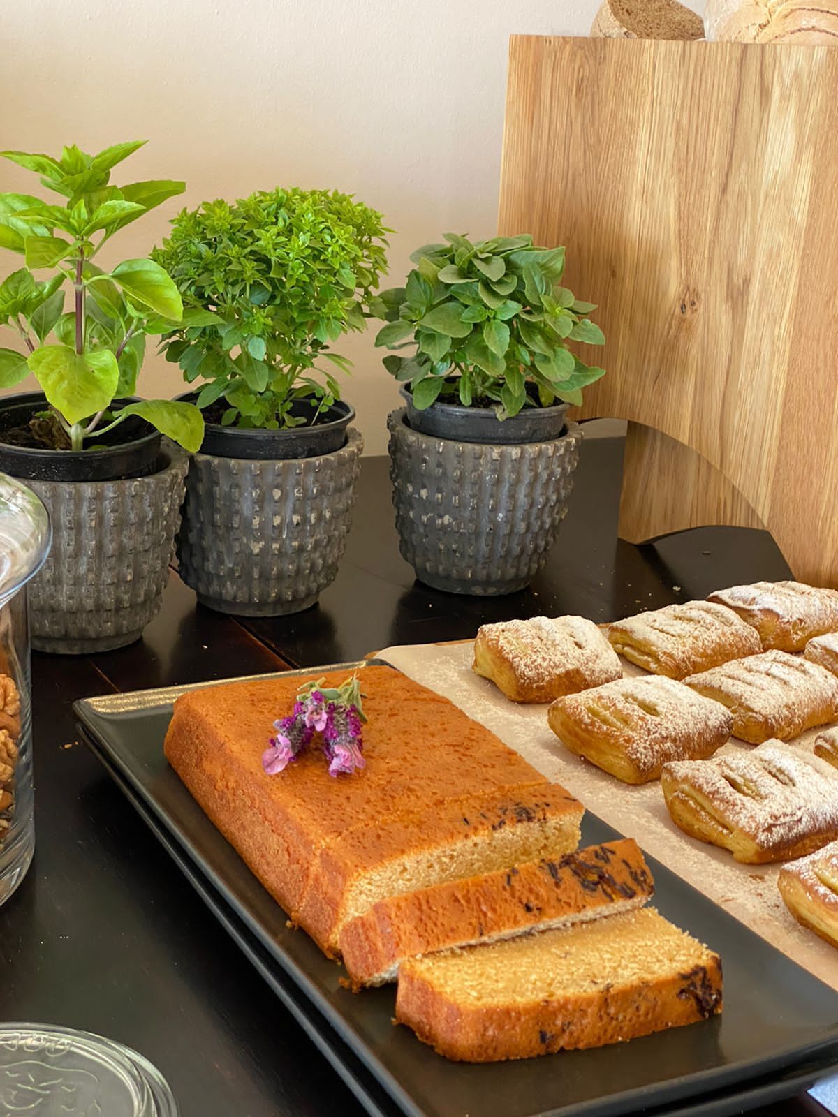 Una mesa con pan, una bandeja de pasteles y plantas en macetas.