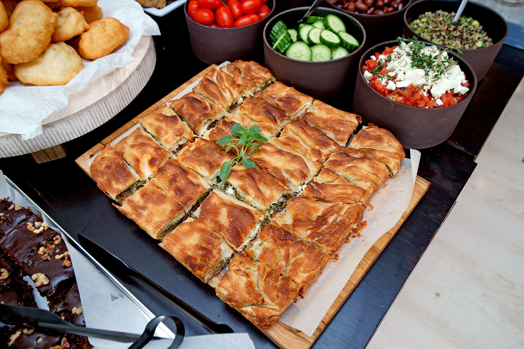 Een schaal gebakken gebak, een kom noten, en verschillende dips en salades op een tafel.