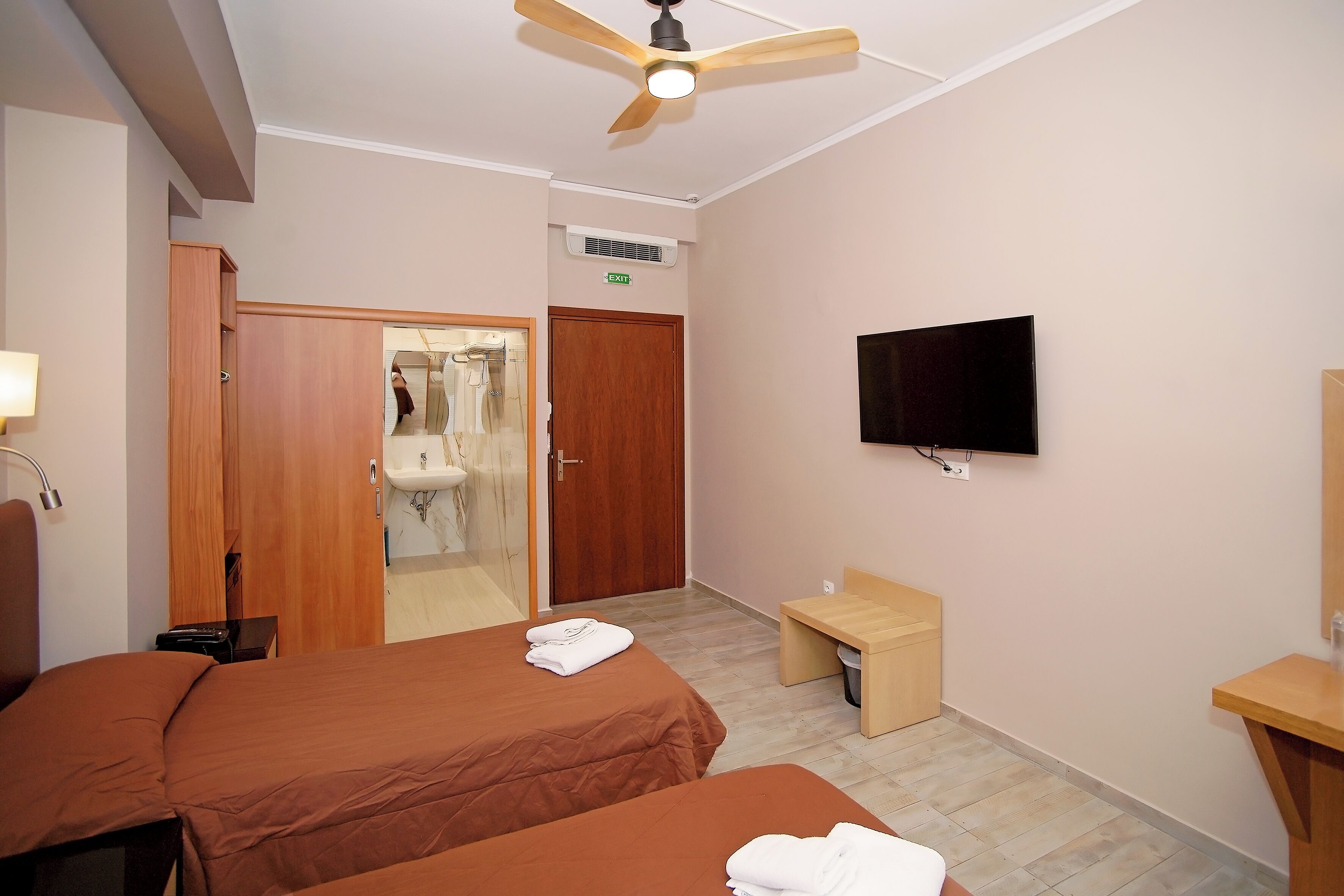 A hotel room with two beds, a ceiling fan, a TV, a sink, and a mirror.