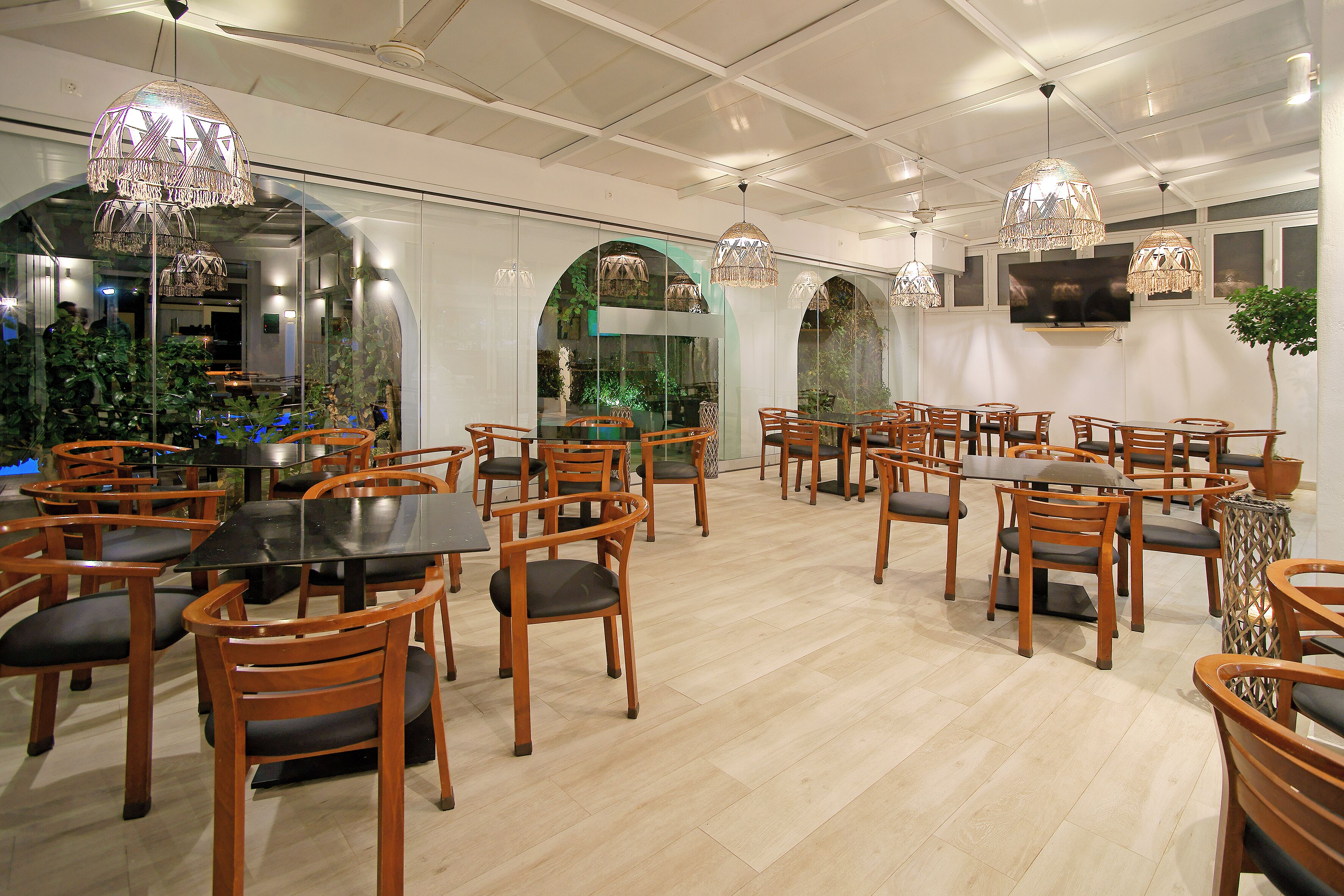 Un comedor amplio con mesas y sillas de madera, ventanas grandes y lámparas decorativas colgantes.