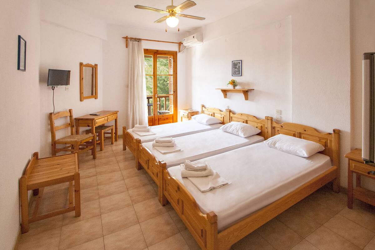 A hotel room with two wooden beds, a desk, chairs, a TV, and a ceiling fan.