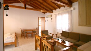 A cozy living room with a wooden ceiling, a sofa, a dining table with chairs, and a bed with neatly made linens. - Pension Eliza (Skiathos)