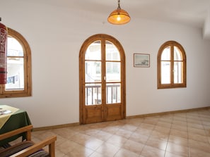 A room with two arched windows, a wooden door, a hanging light fixture, and a tiled floor. - Pension Eliza (Skiathos)