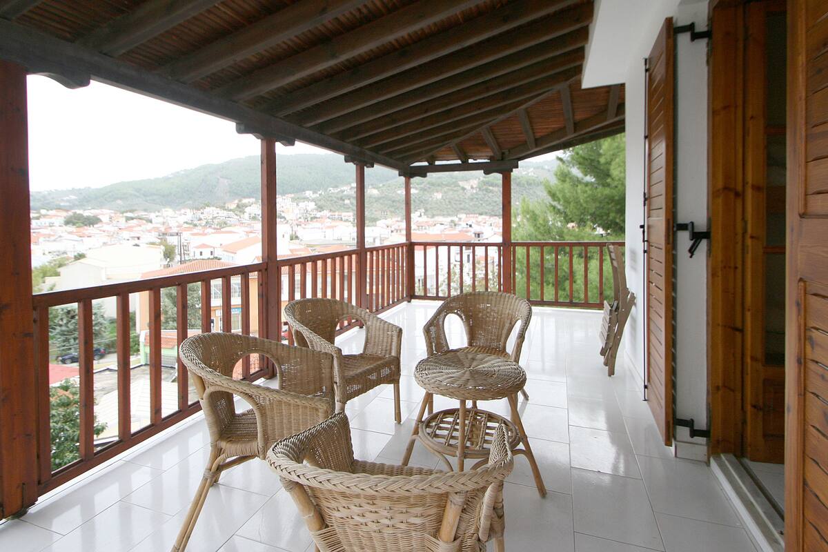 A covered balcony with wicker furniture and a view of a town.