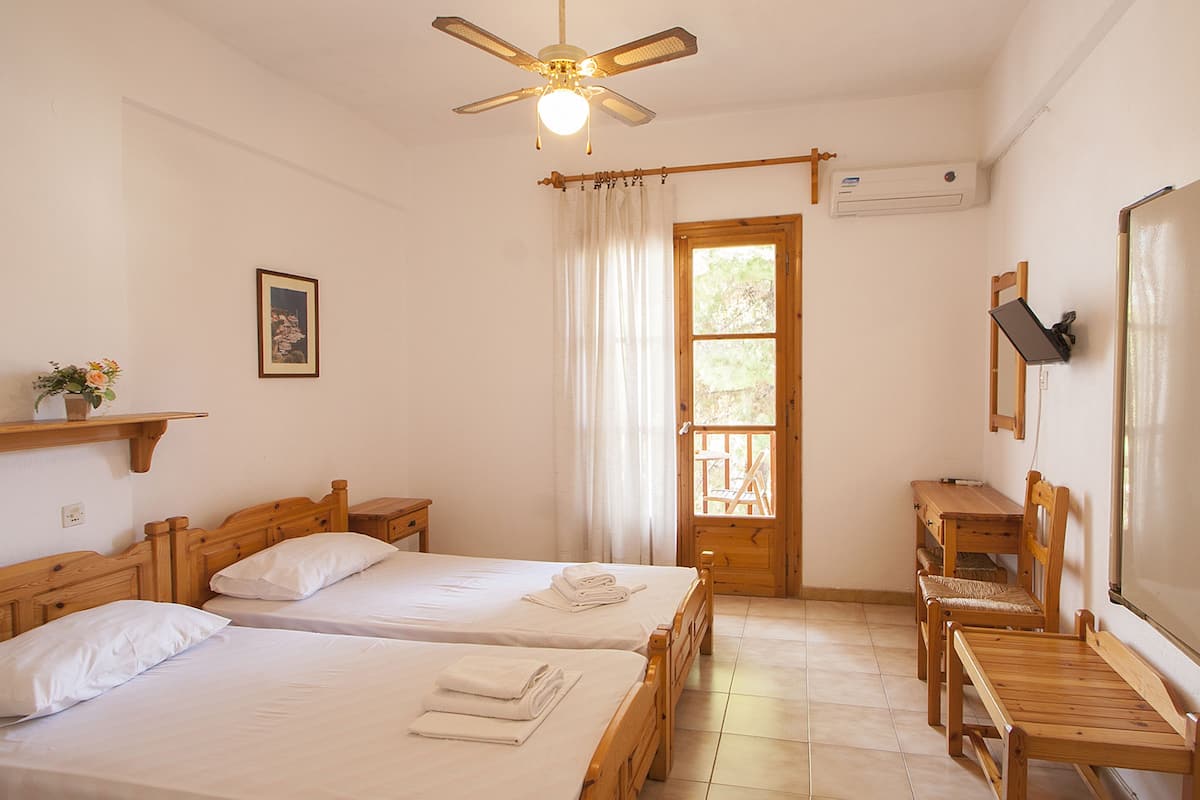 A hotel room with two wooden beds, a ceiling fan, a wooden desk, a chair, and a window with curtains.